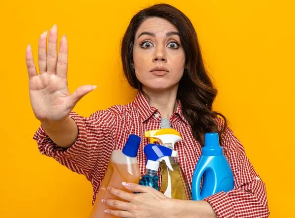 woman holding cleaning spray bottles and holding hand up in a stop sign - COSHH Training