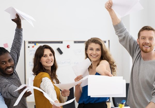 Group of people in classroom holding sheets of paper, smiling, celebrating. CQC Awareness and preparing for the single assessment training.