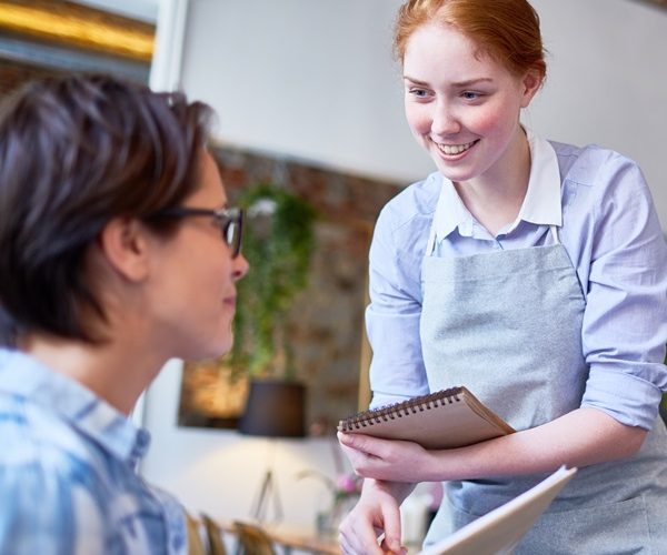 Wait staff serving a client smiling with notebook taking order. Picture for Customer service training course