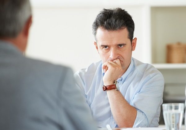 Two people in a meeting. One person looking at other intensely with hand resting on chin. Difficult Conversations training