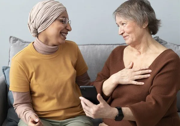 Two people sitting together one holding a mobile phone both smiling. Effective communication and Dementia training.