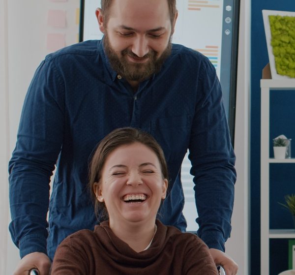 Cheerful young man pushing smiling, laughing person in a wheelchair Leading Change Improving Care training