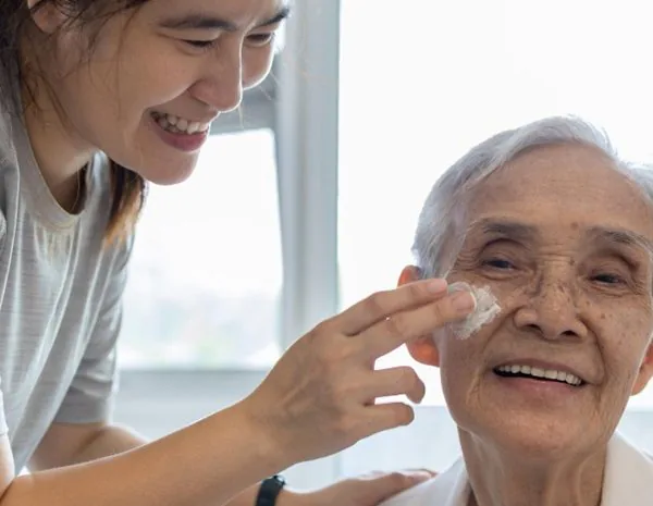 Person applying face cream to an elderly patient's face whilst both smiling and appearing happy Personal Care training