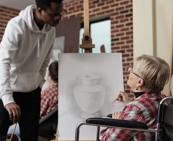 Artist teacher explaining drawing technique to senior woman with disability Using a strengths based approach training