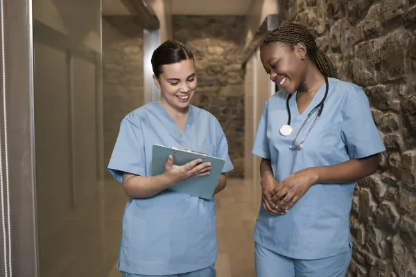 Two nurses working smiling looking at notes. Tracheostomy Care.