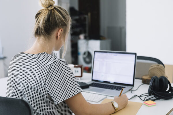 businesswoman sitting in front of laptop at desk making notes understanding the benefits of asc-wds